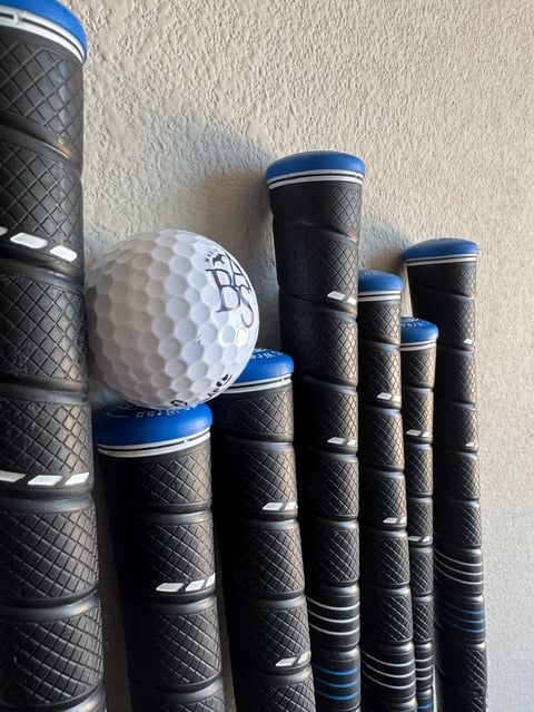 Golf ball resting on top of multiple black and blue golf club grips arranged in a row