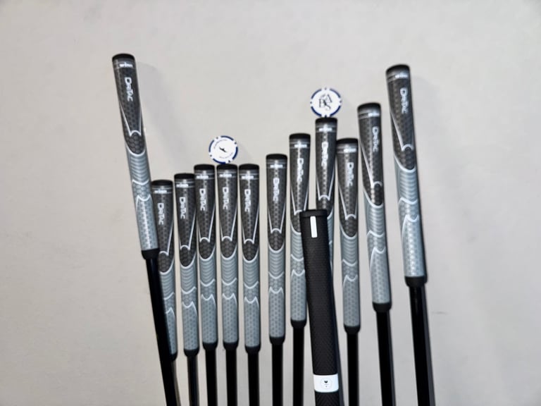 Black and gray golf club irons arranged in a row, showing varied shaft lengths and textured grips